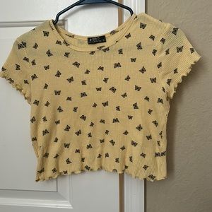 This is a cropped shirt that is yellow with black butterflies